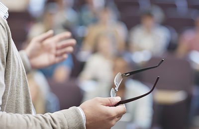 Professor holding eyeglasses and gesturing in lecture hall Professor holding eyeglasses and gesturing in lecture hall